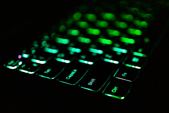 Low key macro of a backlit laptop keyboard isolates glowing modifier keys in emerald and teal. Close perspective and silky bokeh provide texture and room for captions in sleek technology projects.