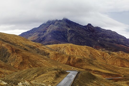 A winding road leads through a mountainous landscape under a cloudy sky, Pajara, Fuerteventura, Canary Islands, Spain