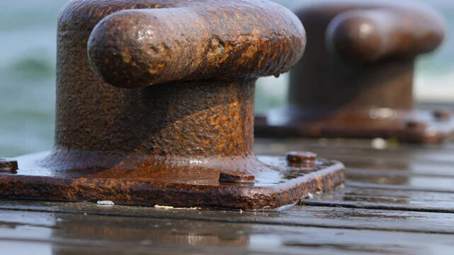 Large rusty metal mooring bollards on wet wooden dock with heavy sea spray splashing over