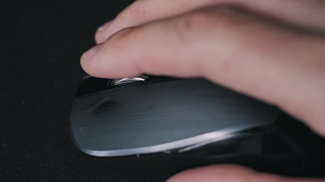 Close-up of a male finger scrolling the textured wheel of a black computer mouse on a brushed metal surface. The user interaction highlights internet browsing and navigation control.