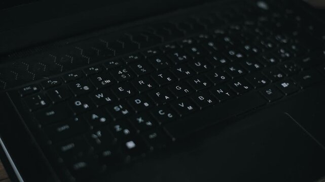 High-angle macro shot of a hand spraying sanitizing liquid on a black laptop keyboard. The subsequent wiping action ensures disinfection and promotes a healthy workspace environment.