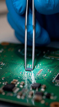 Technician using tweezers to mount microchip on green circuit board in repair workshop