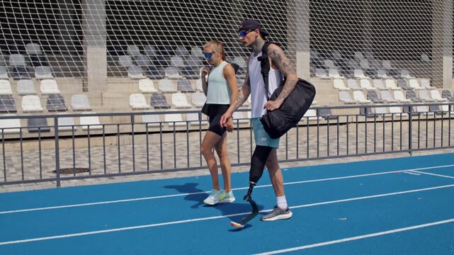 Male runner with bionic leg prosthesis and instructor on track