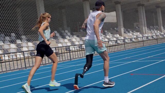 Man with bionic prosthetic leg and female trainer run on track