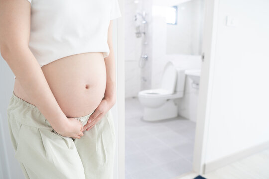 Incontinence and frequent urination during pregnancy. Pregnant woman need to pee standing by toilet in bathroom.