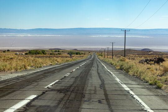 View of a long asphalt road stretching through the arid desert landscape with power lines and distant mountains under a clear blue sky San Pedro de Atacama, Antofagasta, Chile.