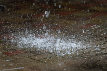 Close up texture view of rainwater hitting stone paving blocks outdoors, creating a crown of water droplets and bubbles in a storm © K