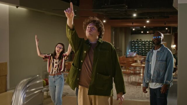 Young Caucasian man throwing bowling ball and celebrating strike with multiethnic friends with high fives and cheering. Marketing campaigns promoting recreational activities and group entertainment