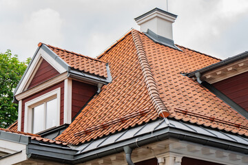 Fototapeta premium Traditional clay tile roofing on a historic wooden building with a detailed dormer window construction and white stucco chimney pipe
