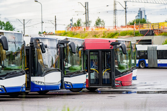 Front view of a public transportation fleet parked in a bus terminal yard near railway overhead wire structures