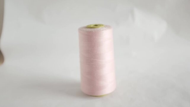 Studio shot of a large spool of pastel pink sewing thread standing upright. Soft and even lighting,  minimalist aesthetic. Sewing, tailoring, fashion design, textile industries, handmade crafts, DIY