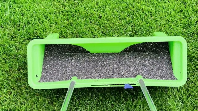 Spreader spreading fertilizer on lush green grass during springtime lawn care maintenance