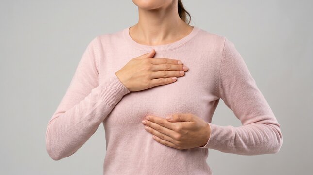 Woman wearing a soft pink long sleeved shirt places her hands gently over her chest for a medical examination