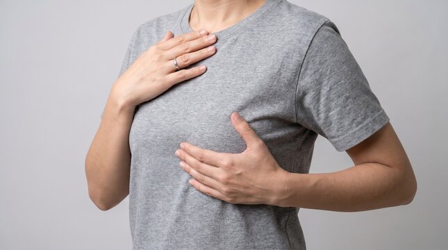 Woman in a casual grey t-shirt performs a self breast examination to check for lumps and ensure her health