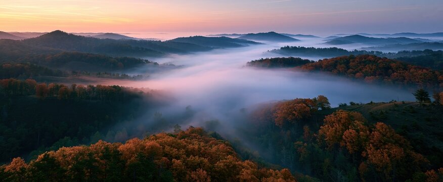 Sunrise over foggy autumn hills with vibrant amber trees showcasing serene natural beauty.
