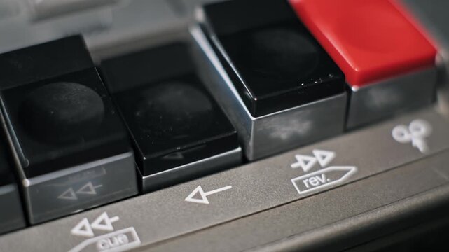 Macro side-angle view of a finger pressing the play key on a classic audio cassette player. The worn black plastic button depresses into the silver control panel.