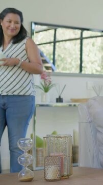 Vertical video: Camera pulling showing woman in top with mug walking at home hourglass, copy space