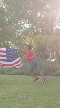 Vertical video: Standing couple in jeans watching boys playing, rushing past yard, waving US flag