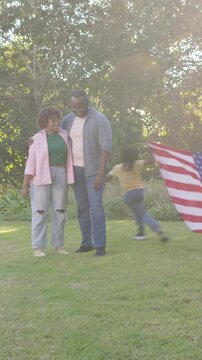 Vertical video: Standing couple watching kids playing with US flag in yard, one child falling