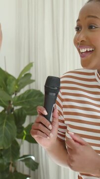 Vertical video: Raising hand, striped woman singing as group waving mics and brush home karaoke