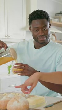 Vertical video: Tilting pitcher man in pastel tee pouring juice at home handing glass for breakfast