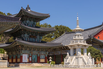 Obraz premium Traditional Korean Buddhist temple architecture with colorful Dancheong paintings and ancient stone pagoda under a clear blue sky.