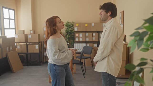 Man and woman smiling with arms crossed beside stacked parcel boxes in a small shipping room in a building; confidence teamwork.