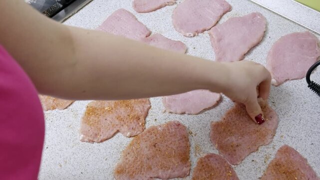 A woman's hand flips seasoned raw pork slices on a speckled kitchen countertop to ensure even marinating. Concept of homemade meal preparation, traditional cooking, and culinary basics.
