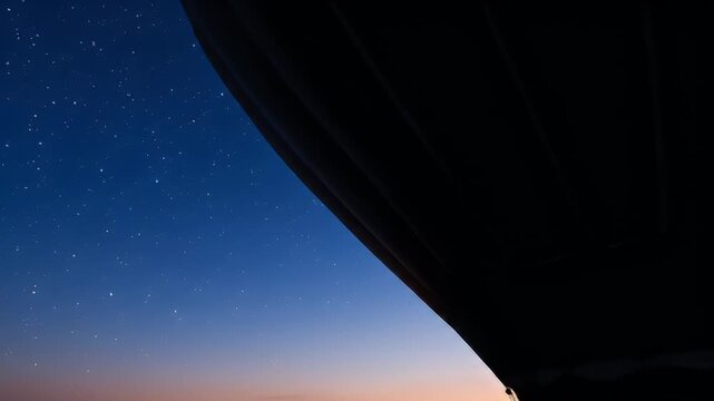 Clear starry night sky seen through dark roof silhouette with soft glowing horizon gradient