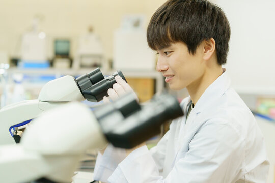 顕微鏡で作業をする白衣を着た若い日本人男性　実験　研究　開発　勉強　
撮影協力：学校法人電波学園 東京電子専門学校
