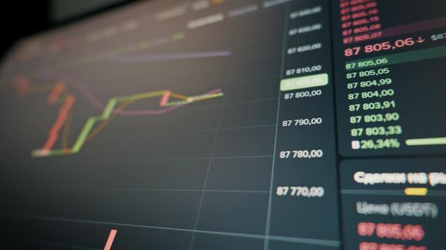 Digital screen shows a real-time cryptocurrency price chart and order book with fluctuating numbers. The dark background emphasizes the glowing green and red financial data on the trading platform.
