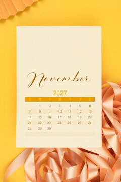 November 2027 calendar page with yellow ribbon on yellow background.