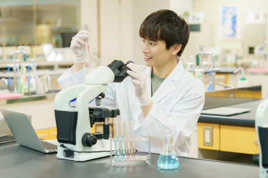 顕微鏡で作業をする白衣を着た若い日本人男性　実験　研究　開発　勉強　
撮影協力：学校法人電波学園 東京電子専門学校
