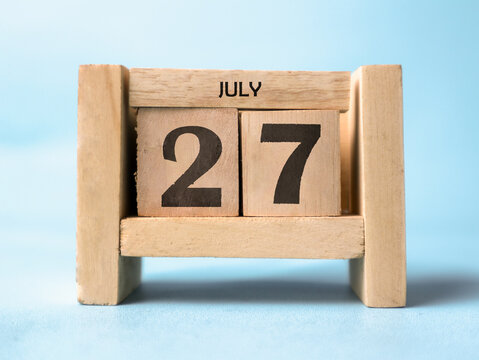 A wooden block calendar for July twenty-seventh on a light blue background.