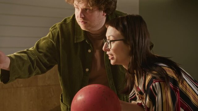 Young Caucasian man and woman playing game of bowling, aiming, throwing ball then celebrating success with high five and hug. Perfect for promoting recreational activities, dating apps, or friendship