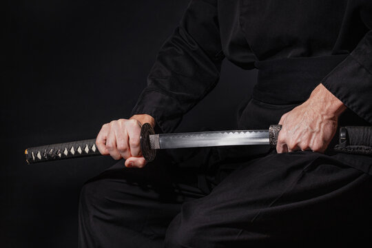 The samurai holding a Japanese katana sword. Photo of a warrior dressed in black clothes in low key with selective