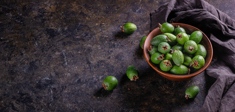 Tropical fruits green ripe feijoa sellowiana berries in a clay bowl and on a table on a dark background. Kitchen banner with copy space for text