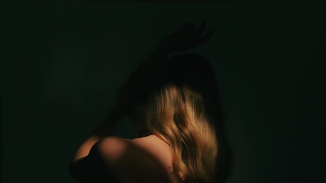 Woman with long blond hair in a dark room playing with light casting shadows on her face