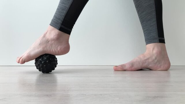 A woman uses a massage ball to relax her feet. Relieves muscle tension, reduces puffiness and relieves fatigue after a long walk. Close-up
