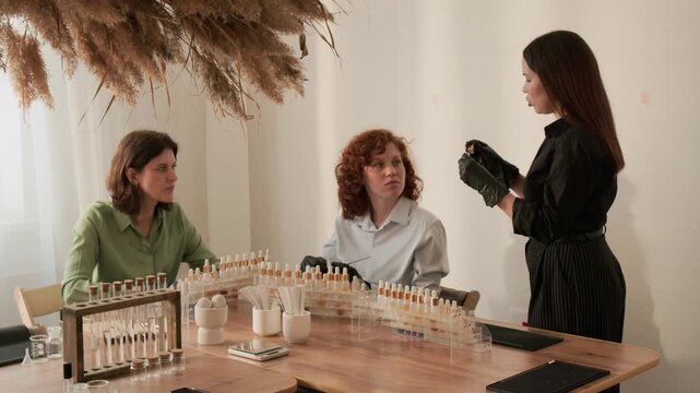 Caucasian female instructor teaching perfume making masterclass to young adult women, letting them smell scent strip. Perfect for promoting beauty education or cosmetic brand marketing