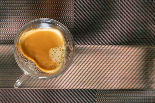 Top view of a fresh cup of espresso coffee with rich crema in a glass mug with copy space on a textured placemat.