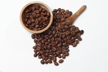 Fototapeta premium A pile of roasted coffee beans with a bowl and a small wooden spoon on a clean white background. Perfect for design elements, organic culinary themes, and the coffee industry.