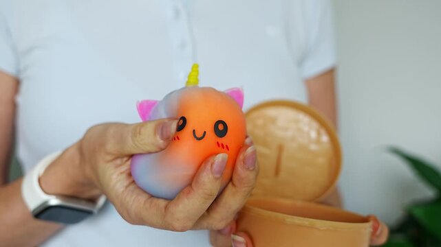 Woman holding and squeezing cute unicorn squishy bun toy in hands. Sensory stimulation and stress relief concept.