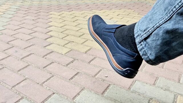 Close up of a man s leg wearing a casual blue loafer while standing on pavement outdoors. Stylish footwear detail, urban fashion concept, everyday lifestyle and street scene