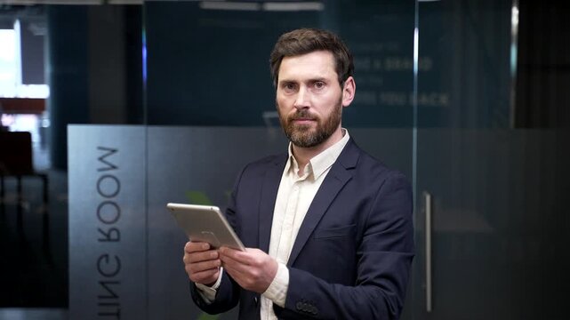 Portrait of serious confident businessman in formal suit using digital tablet in office. Focused professional manager looking at camera after reviewing data, symbolizing leadership, authority, success