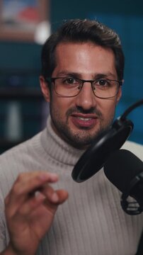 Portrait of happy man tells interesting story during podcast show in audio studio vertical shot. Host with glasses conducts talk show in multimedia office