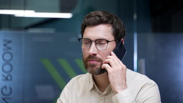 Close-up of businessman talking on smartphone in office. Confident professional discussing work matters with client or colleague, making business call and managing corporate communication at workplace