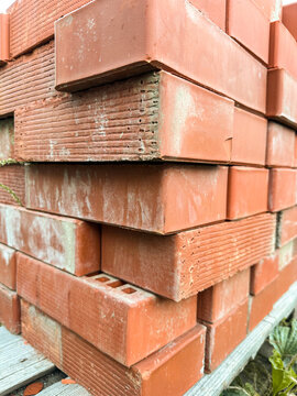 New red perforated brick pallets wrapped in plastic on a construction site.