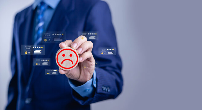 Businessman holding sad face icon with low customer rating and negative reviews. Customer dissatisfaction, poor service experience, complaint management, reputation risk and feedback concept.
