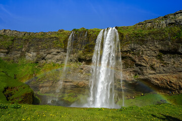 A majestic waterfall cascades down a rocky cliff into a lush green valley under a clear blue sky,Seljalandsfoss,Iceland © SHUNJI ZHOU
